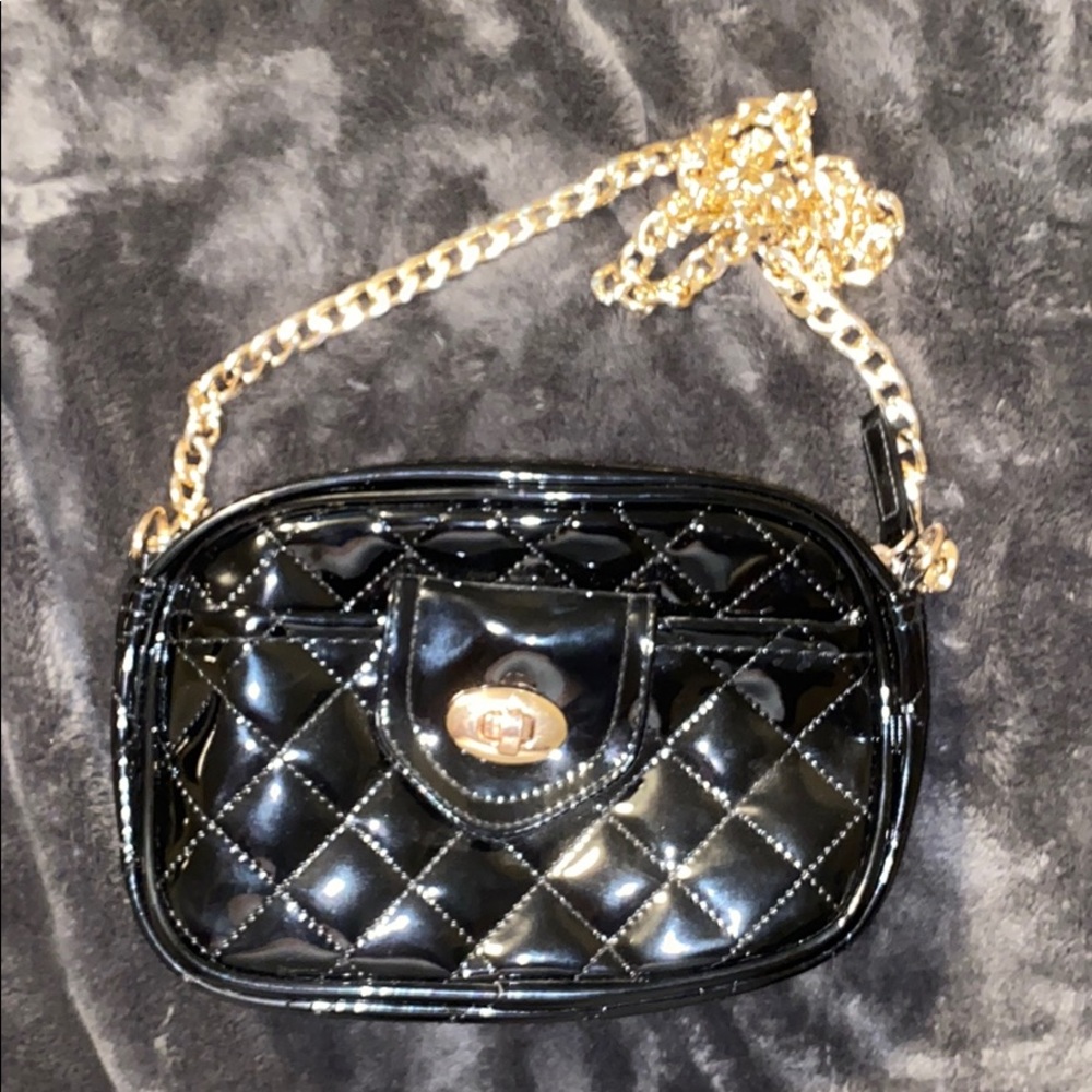 An all black purse with a gold chain as the strap